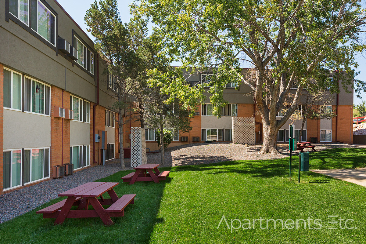 Apartment courtyard with green lawn, picnic tables, and residential buildings.