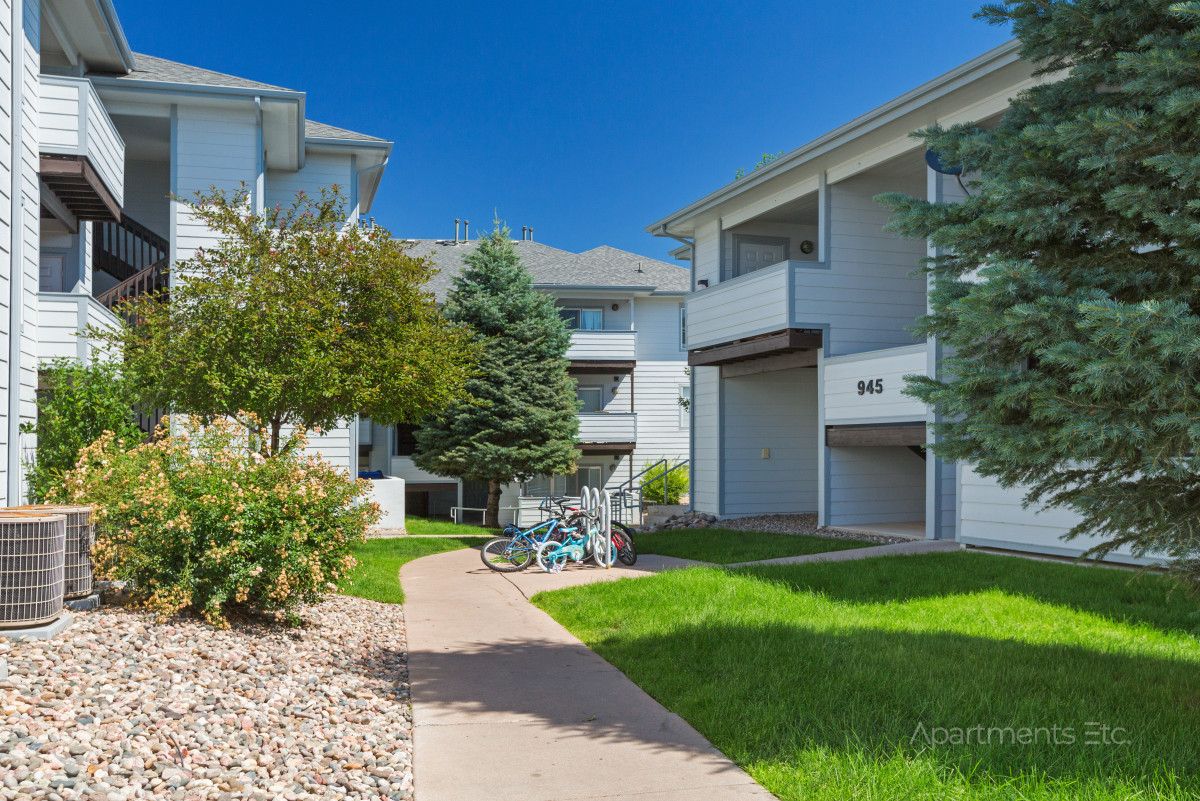 Exterior view of Hillside Pointe apartment community with landscaped walkway and residential buildings in summer.